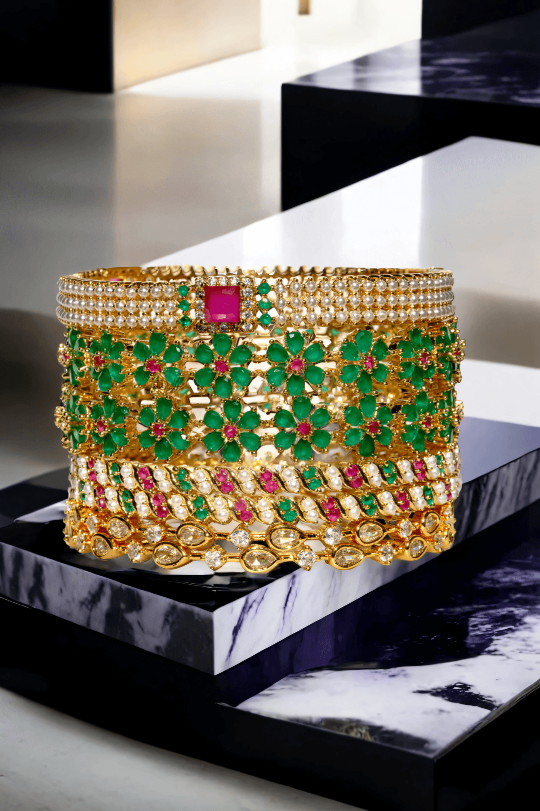 Arika 7-piece floral gold-plated bangle set with emerald and ruby stones on a marble background from Inaury