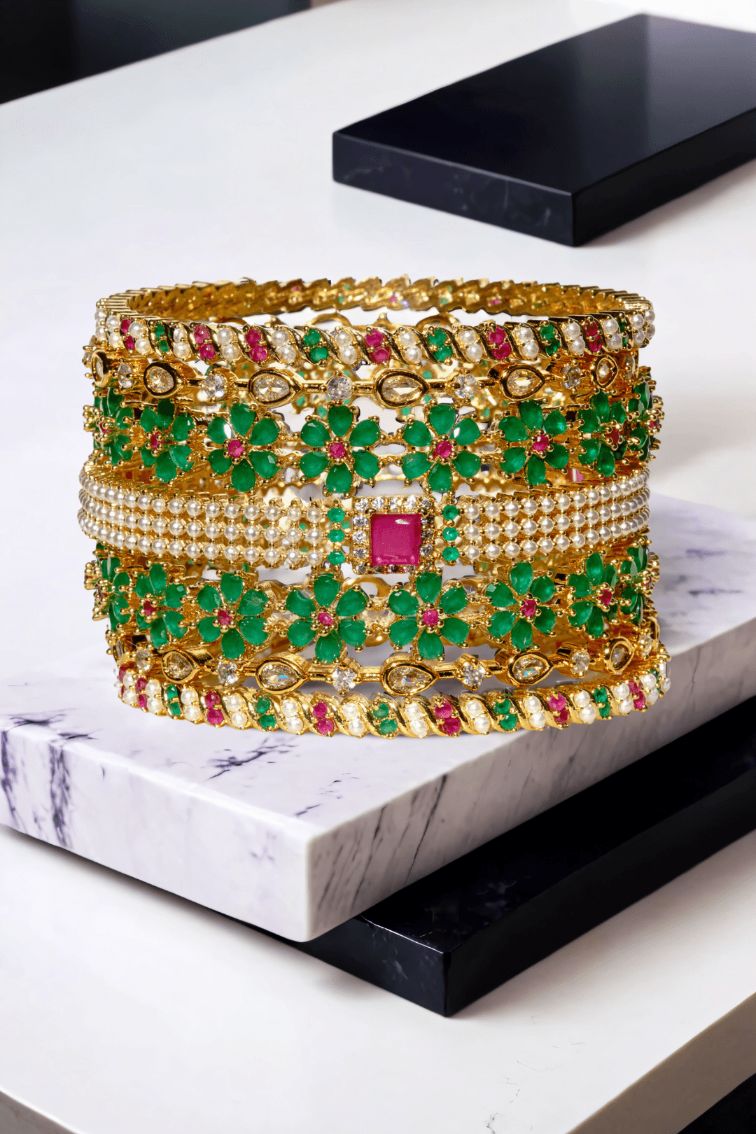 Arika 7-piece floral gold-plated bangle set with emerald and ruby stones on a marble background from Inaury