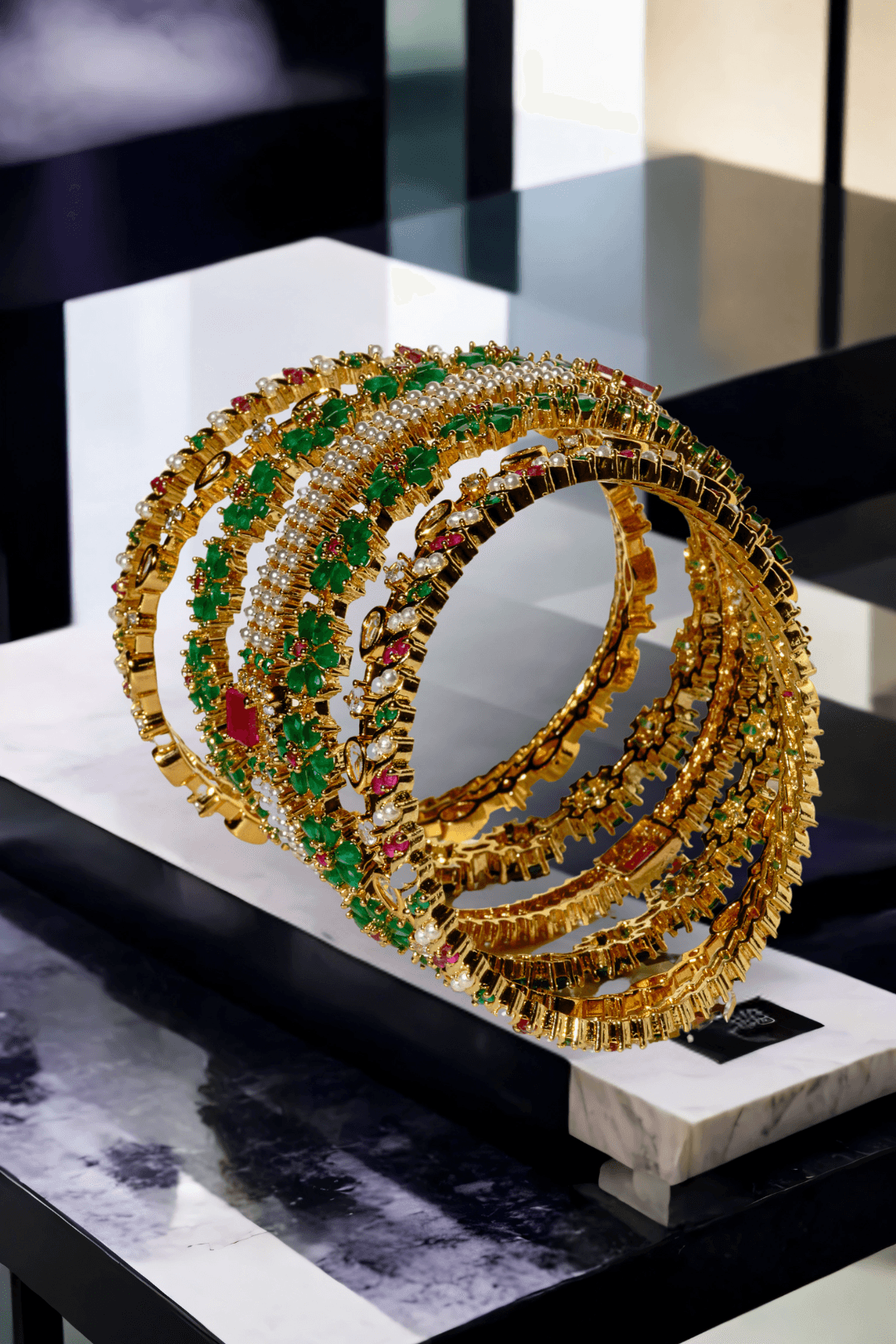 Arika 7-piece floral gold-plated bangle set with emerald and ruby stones on a marble background from Inaury