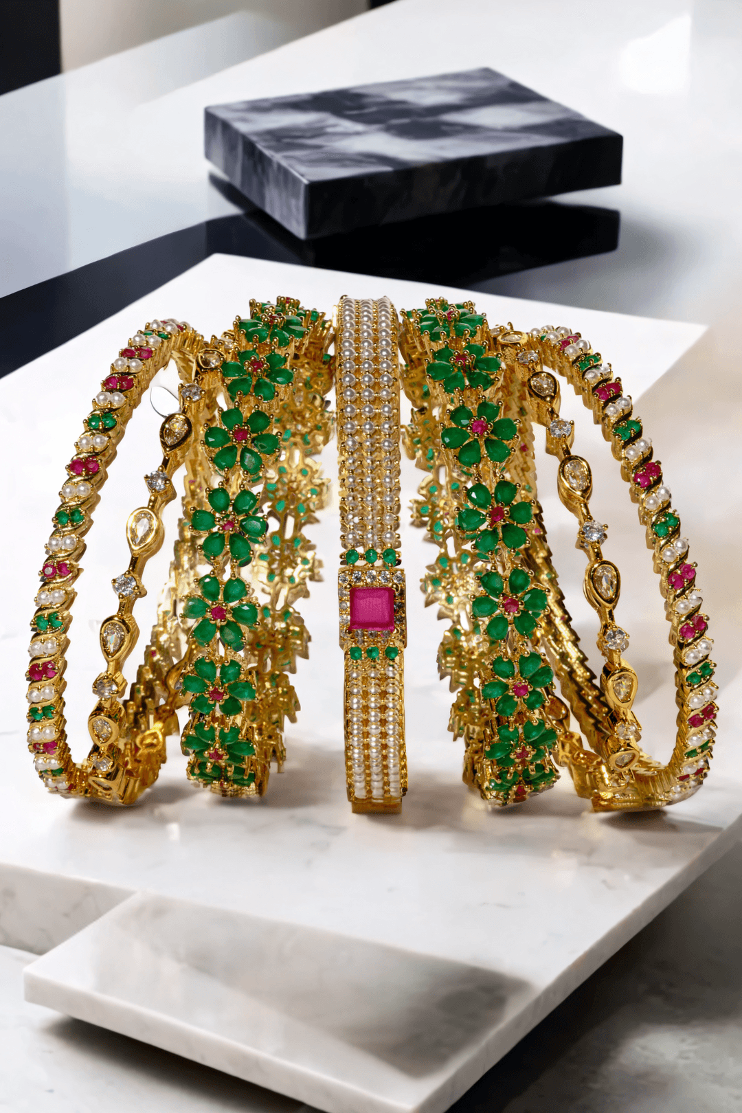 Arika 7-piece floral gold-plated bangle set with emerald and ruby stones on a marble background from Inaury